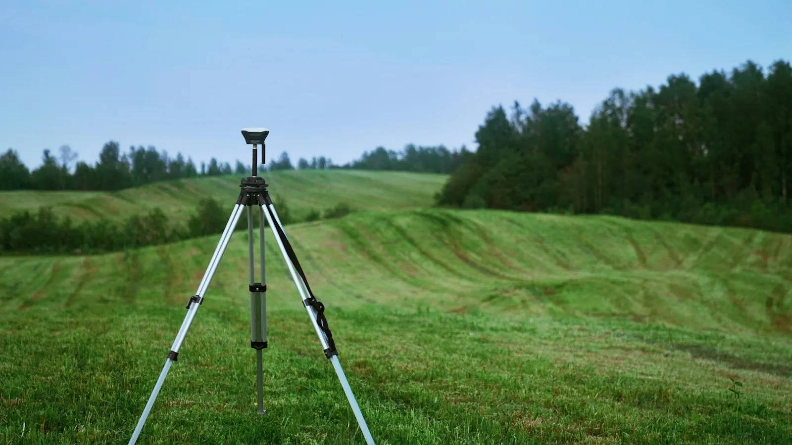 GNSS receiver on a tripod in a rolling meadow during a topographic survey